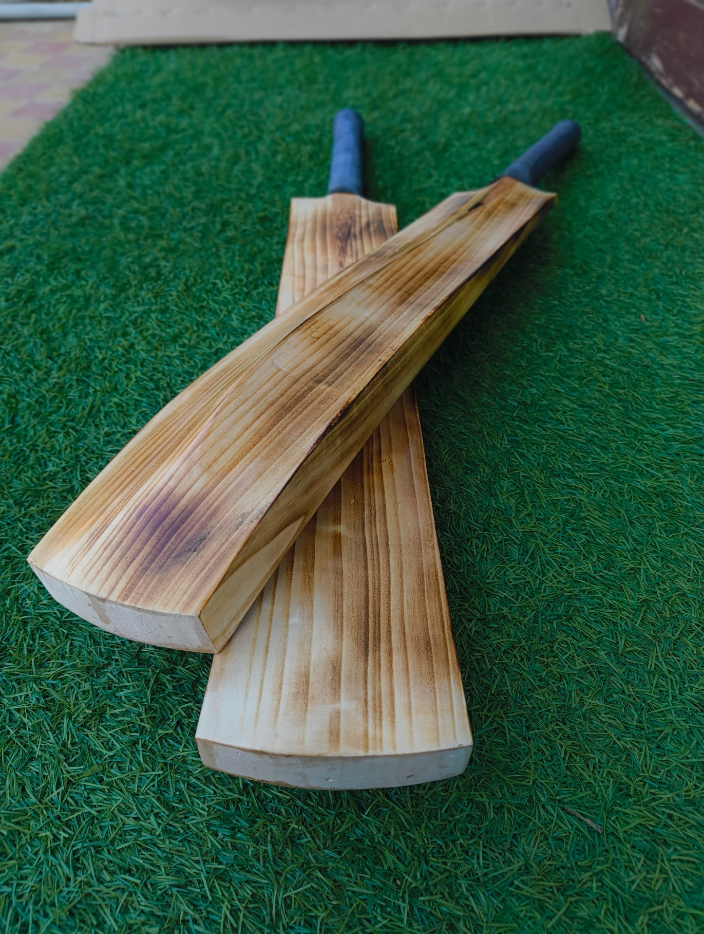 Two wooden hard tennis cricket bats on a green grass-like surface
