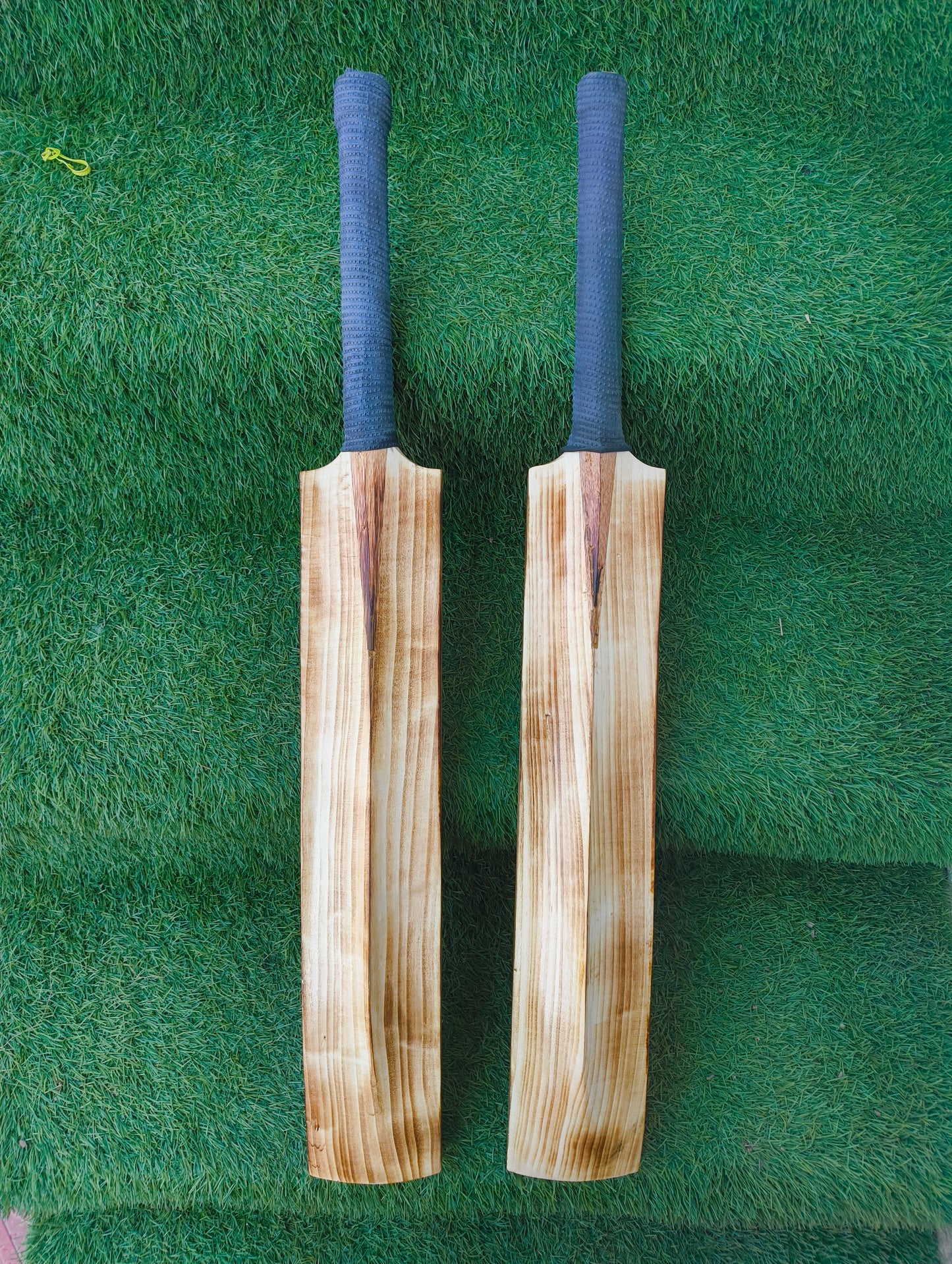 Two wooden cricket bats with blue covers on a green grass background
