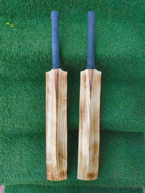 Two wooden cricket bats with blue covers on a green grass background
