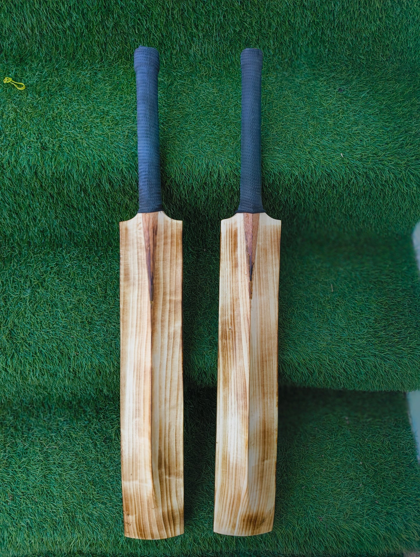Two wooden cricket bats with blue grips on a green grass background