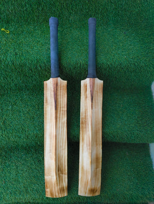Two wooden cricket bats with blue grips on a green grass background